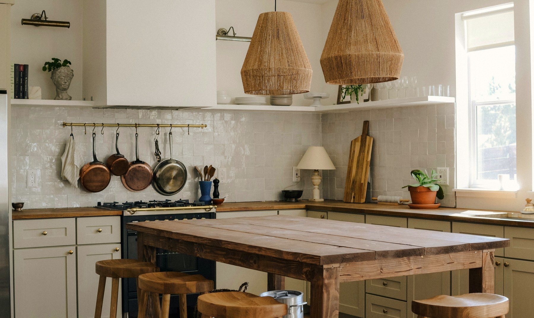 A sunlit kitchen with a wooden island and hanging copper pans.