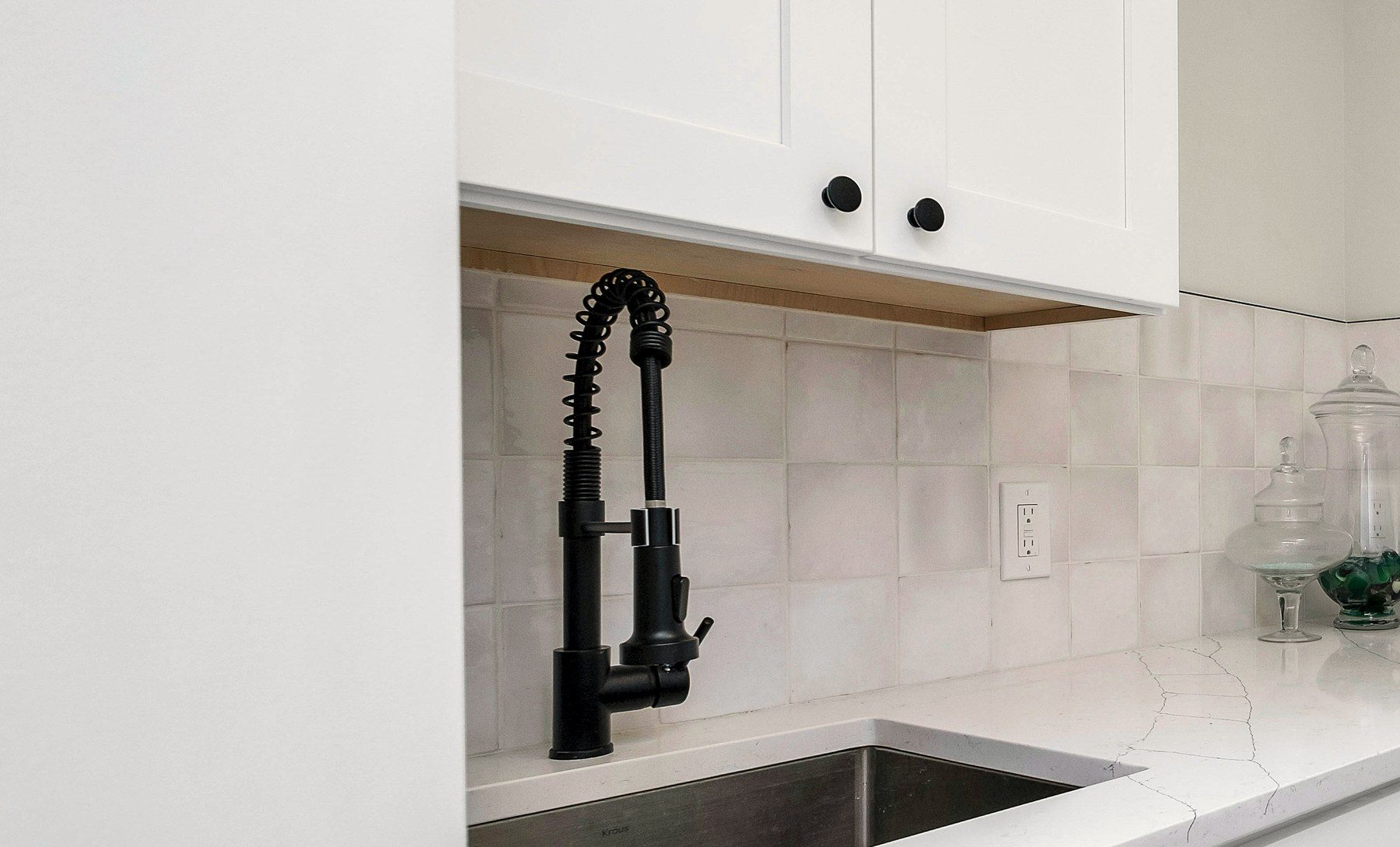 A clean utility sink with a matte black faucet and tiled backsplash.